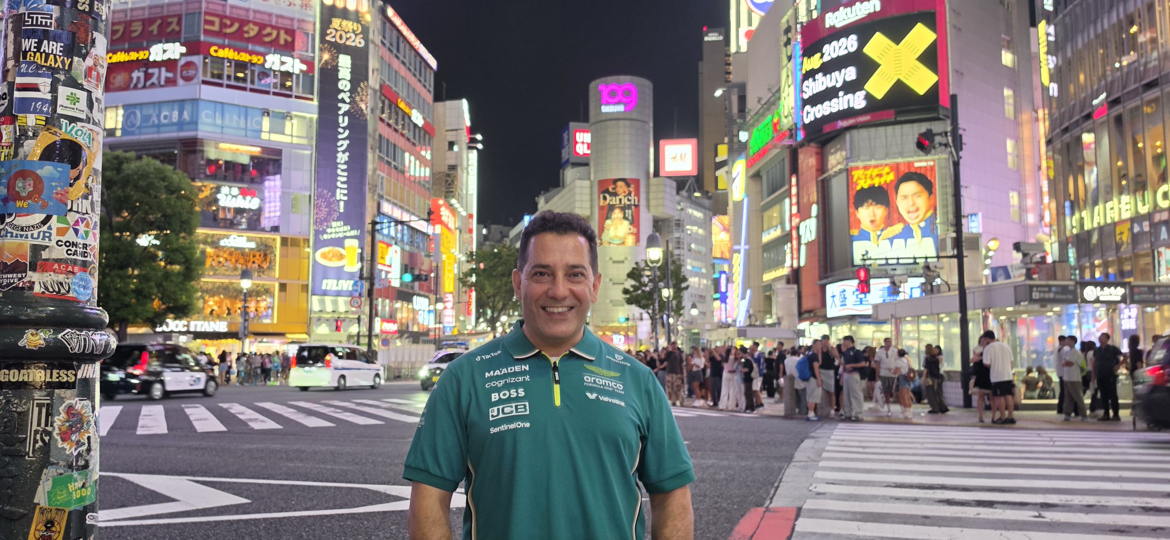 Cam Sourani smiling at Shibuya Crossing in Tokyo at night, neon billboards behind him